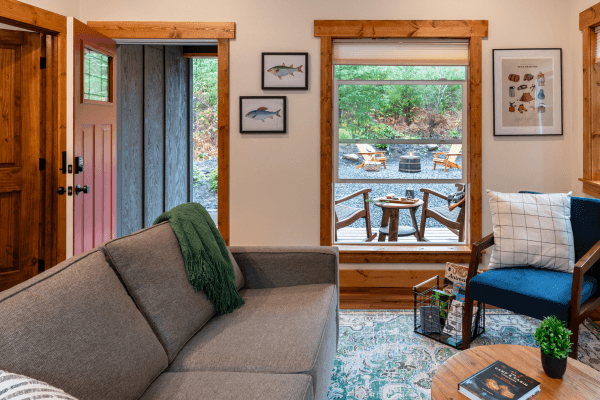 Cabin living area with a sofa, fireplace, wood accents, and large windows with views of the trees.