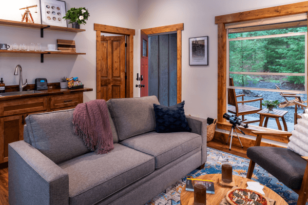 Cabin living area with a sofa, kitchenette, wood finishes, and a window overlooking the trees.
