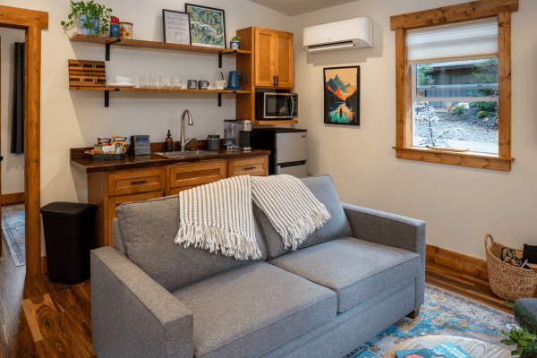 Cabin living area with a sofa, kitchenette, wood finishes, and a window overlooking the trees.