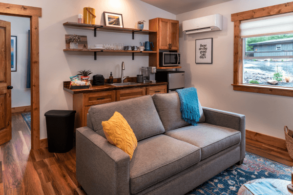 Cabin living area with a sofa, kitchenette, wood finishes, and a window overlooking the trees.