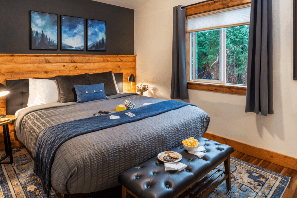 Cozy cabin bedroom with a neatly made bed, warm wood accents, soft lighting, and peaceful forest views through the window.