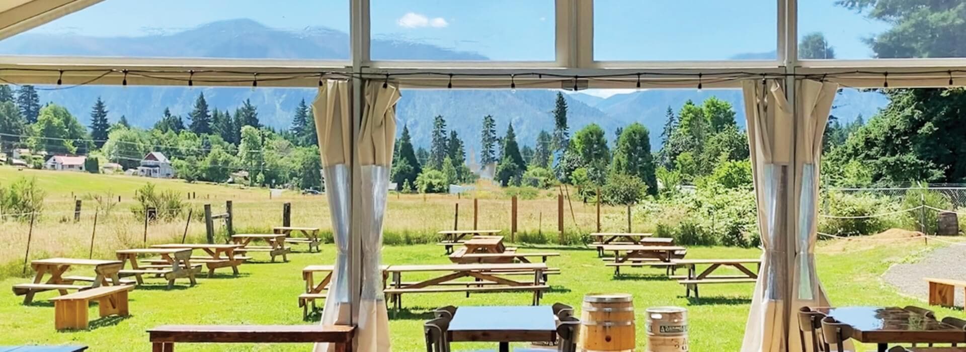 A view from inside a tent overlooking a grassy field with picnic tables and mountains in the background.